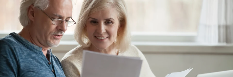 Couple de seniors souriants consultant ensemble des documents papier dans un int&eacute;rieur lumineux pr&egrave;s d'une fen&ecirc;tre
