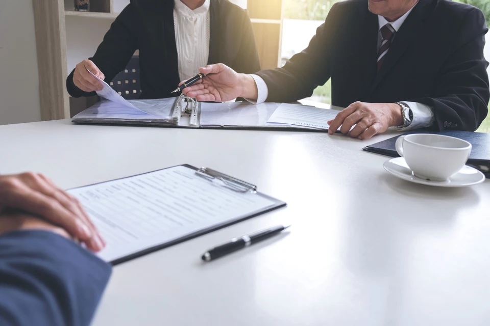 Réunion d'affaires dans bureau moderne avec trois professionnels en costume analysant documents contractuels