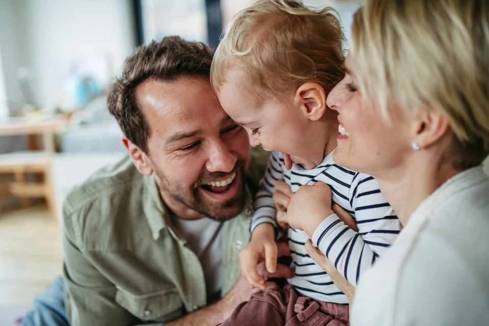 Deux mains protectrices forment un toit au-dessus de pictogrammes familiaux noirs représentant un couple avec enfant et personne âgée avec canne